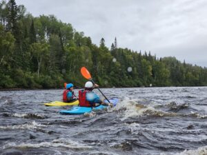 Personne dans un kayak qui apprend le Kayak en eau vive avec un instructeur de l'institut de Kayak Ho'omau